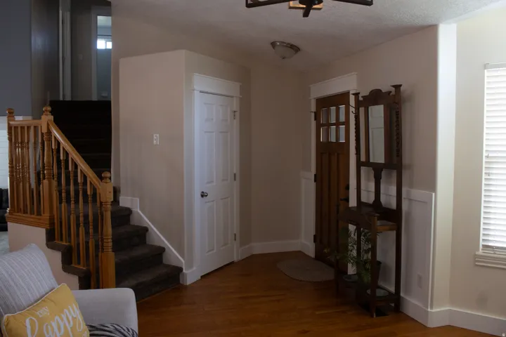 Hardwood flooring with a natural finish, solid panel interior door, wood staircase with balusters, and wainscoting