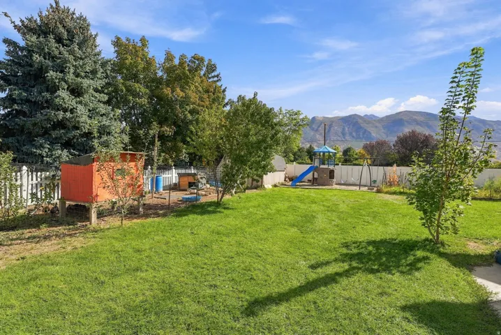 Expansive green lawn with mountain backdrop, established perimeter trees, and white picket fencing