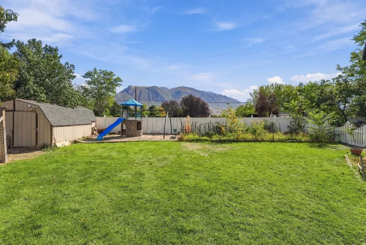 Expansive backyard featuring a manicured lawn, a detached storage shed, and a white privacy fence