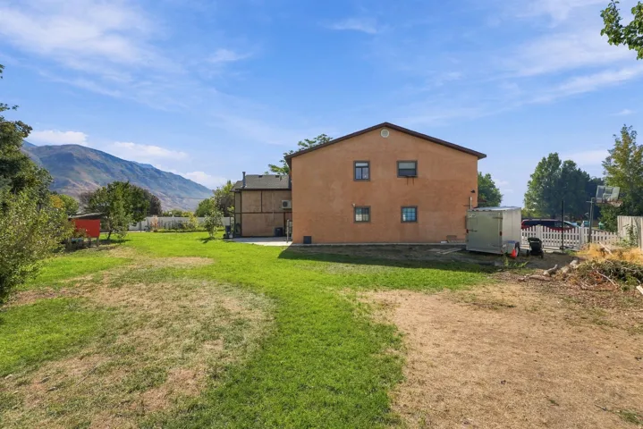 Expansive yard featuring a partial grass lawn, mountain backdrop, and a white picket fence