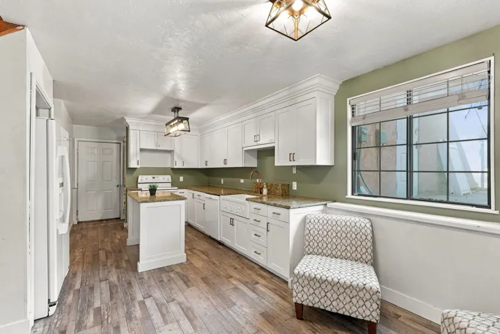 Kitchen featuring wood-finish flooring, white cabinetry, a built-in range, and a central island with a granite-style countertop
