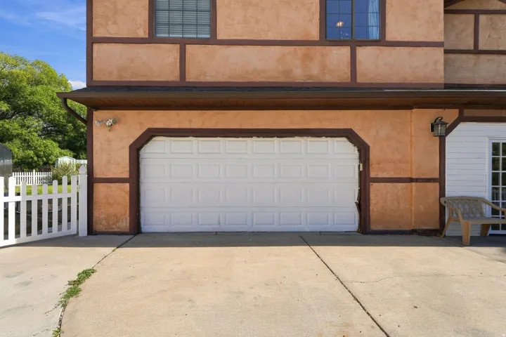 Exterior featuring a single-car garage, stucco siding with timber accents, and a white picket fence