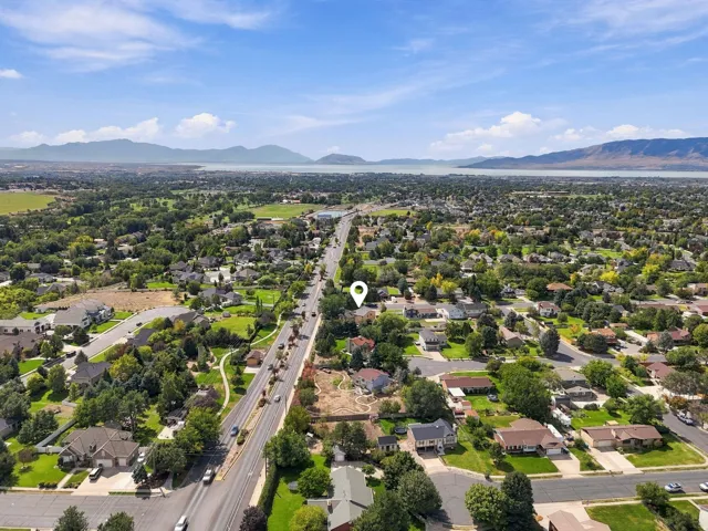 Expansive aerial perspective showcasing a residential neighborhood with established homes, tree-lined streets, distant mountain ranges, and a prominent body of water