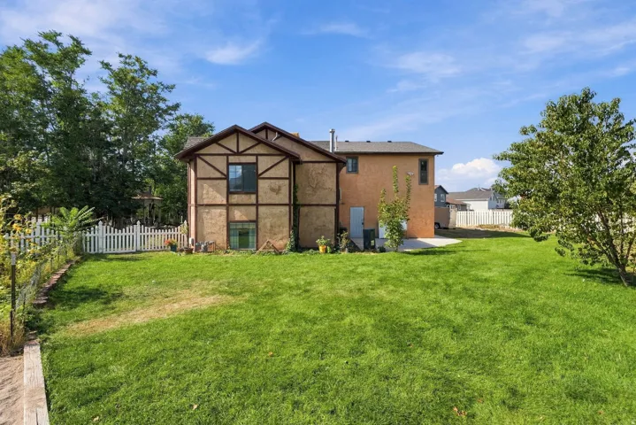 Expansive rear yard featuring a manicured lawn, established landscaping, and a white picket fence