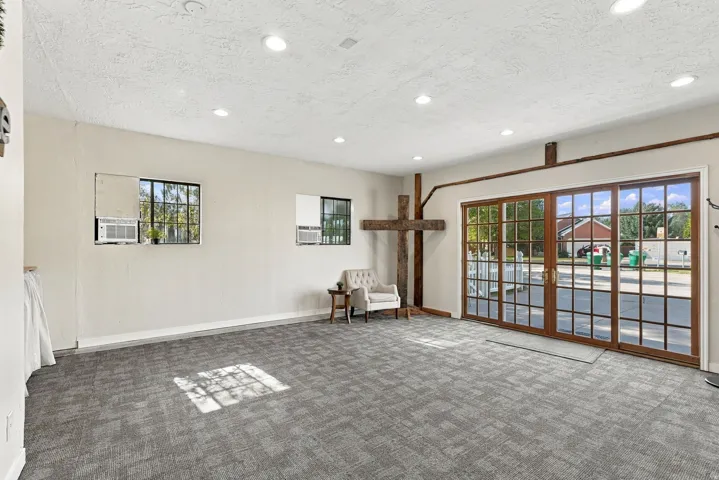Recessed ceiling lighting, wood-finish sliding glass doors, multiple transom windows, textured ceiling, and gray patterned carpet