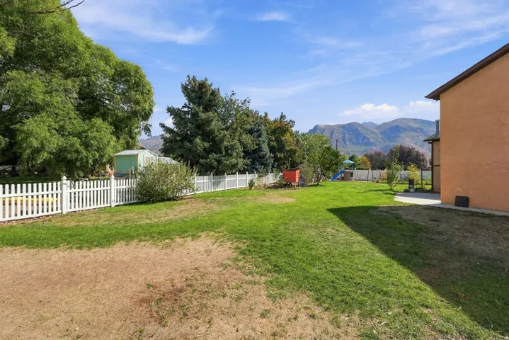 Expansive lawn area, mature trees, white picket fencing, and concrete patio
