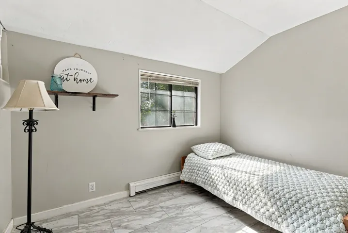Light gray wall paint, white trim, window with blinds, baseboard heating, and light-toned marble-look flooring