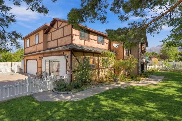 Tudor-style exterior with stucco and timber detailing, attached two-car garage, white picket fence, concrete driveway, and expansive lawn area
