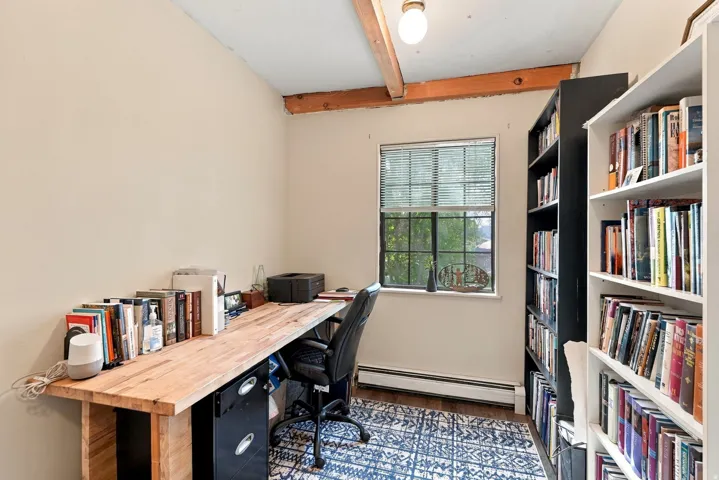 Exposed wood ceiling beams, single light fixture, window with blinds, wood-finish flooring
