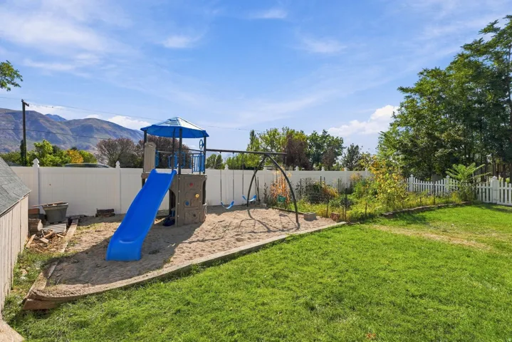 Expansive grassy yard with a white privacy fence, an additional white picket fence, and mature trees