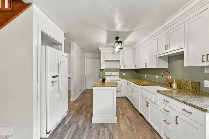 Kitchen featuring white cabinetry, granite countertops, a farmhouse sink, a central island, and wood-finish flooring
