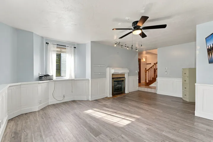 Wood-finish flooring, wainscoting, an electric fireplace with mantel, a ceiling fan, and track lighting