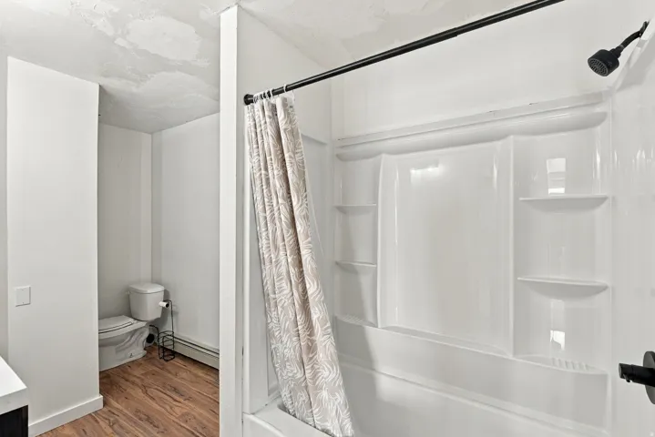 White shower-tub combination unit with integrated shelving, matte black showerhead, and wood-finish flooring