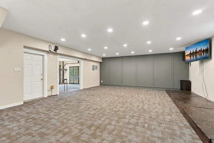 Recessed ceiling lighting, patterned carpeting, paneled accent wall, and a raised wood-finish platform