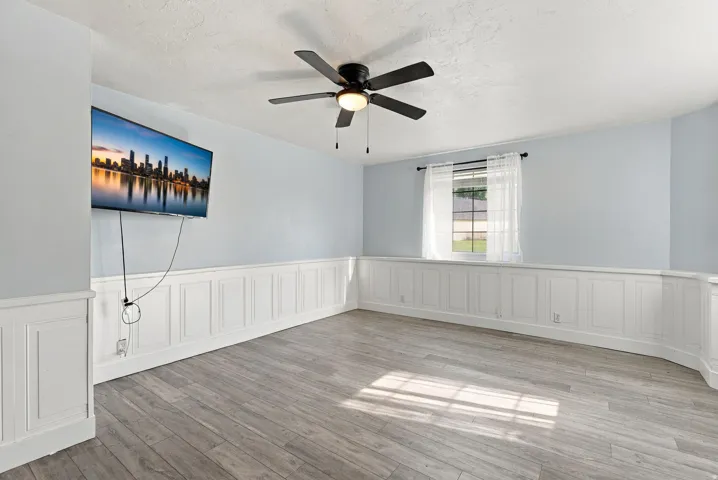 Wood-finish flooring, wainscoting, ceiling fan with integrated lighting, and a single window