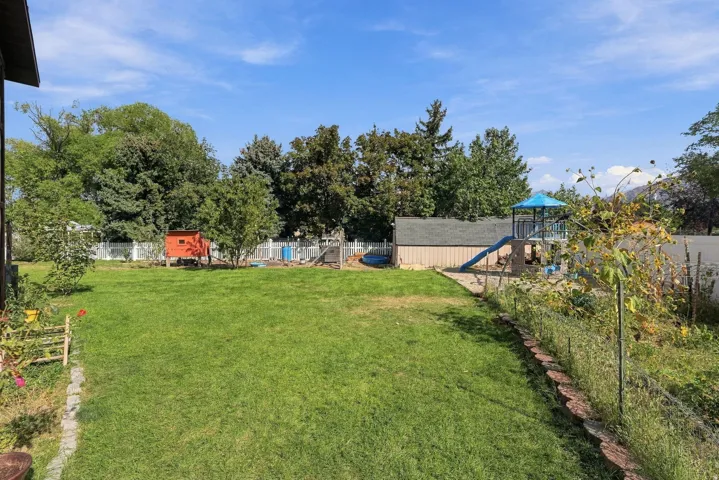 Expansive grassy yard with a storage shed, white picket fence, and mature trees