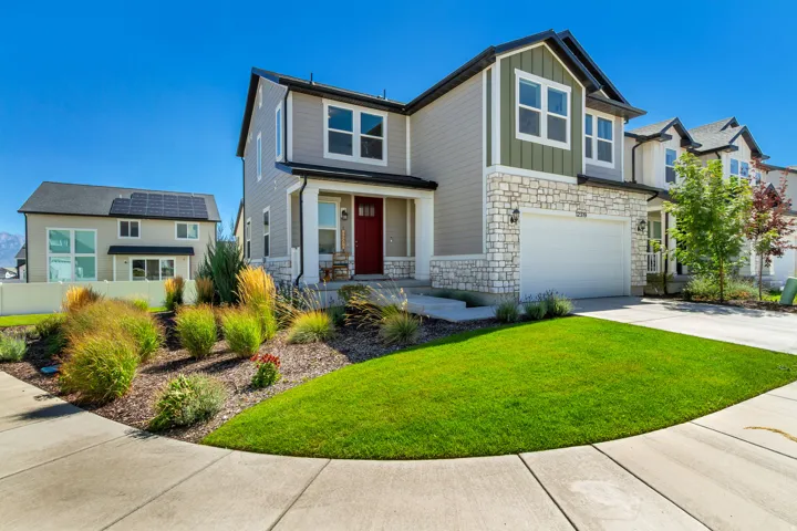 Two-story residence featuring a covered entry, stone and siding exterior, attached garage, and landscaped front yard