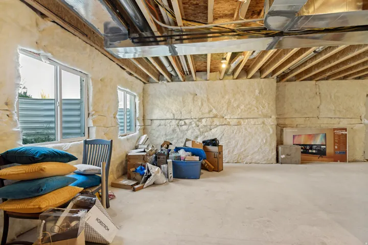Unfinished basement with exposed ceiling joists, concrete flooring, spray foam insulated walls, and multiple windows providing natural illumination