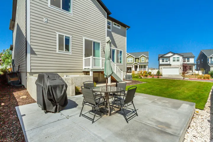 Expansive rear yard featuring a large concrete patio, manicured lawn, and a sliding glass door