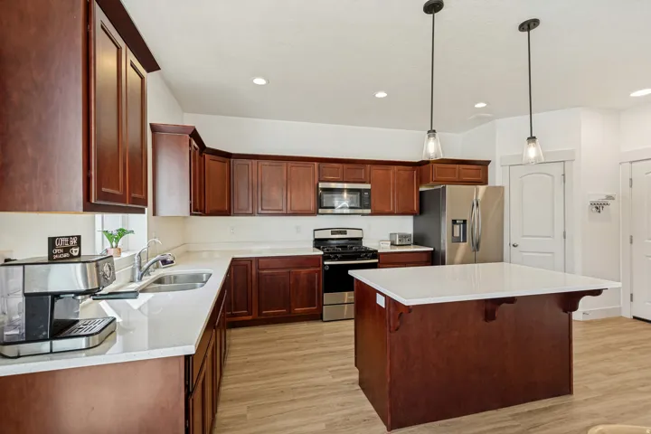 Expansive kitchen featuring a central island with a white countertop, rich wood-finish cabinetry, stainless steel appliances, and wood-finish flooring