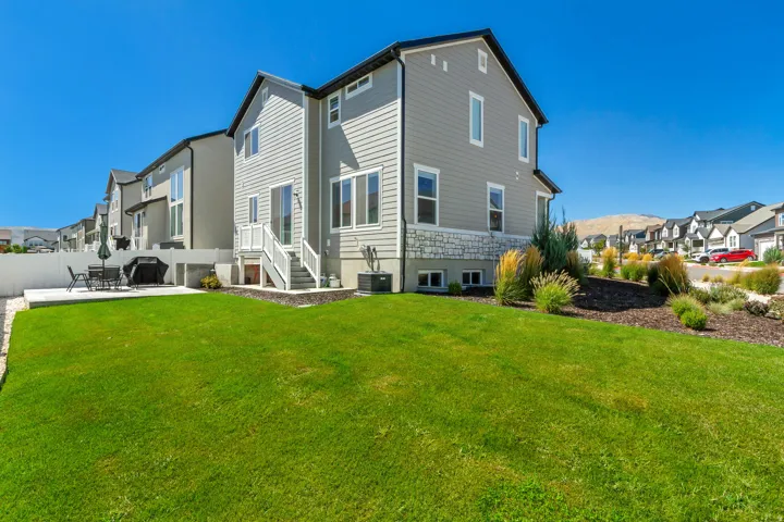 Expansive rear yard featuring a manicured lawn, concrete patio, and mature landscaping