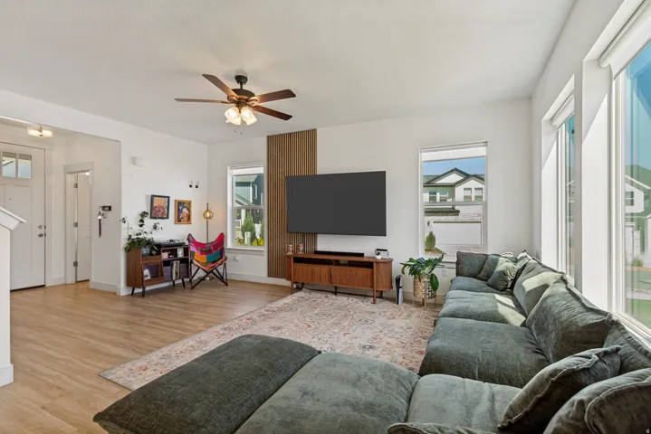 Open-concept living area featuring wood-finish flooring, a ceiling fan with integrated lighting, and multiple windows