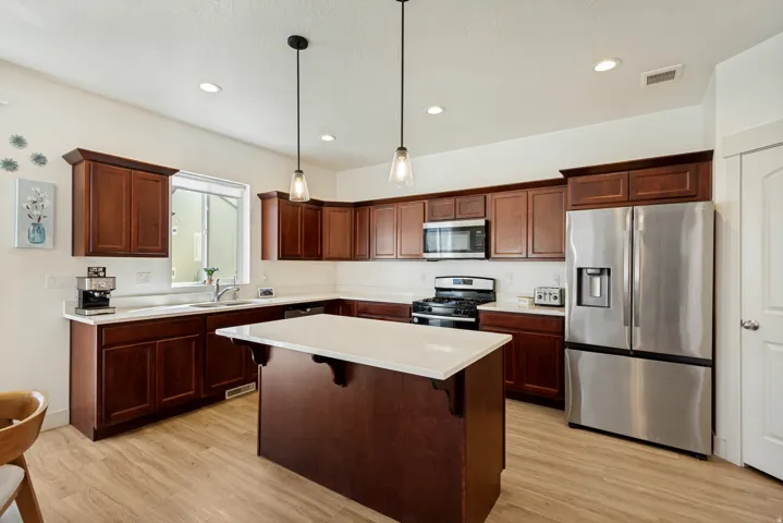 Kitchen featuring wood-finish flooring, dark wood cabinetry, white countertops, stainless steel appliances, and a central island with pendant lighting