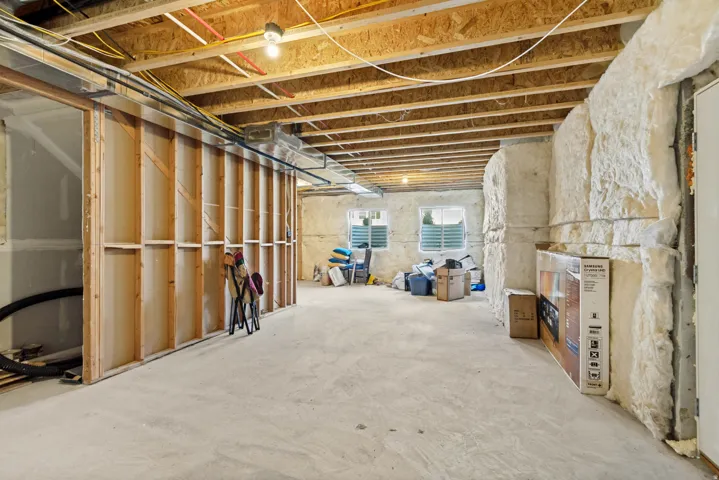 Unfinished basement featuring exposed wood joists, concrete flooring, framed wall partitions, and multiple windows