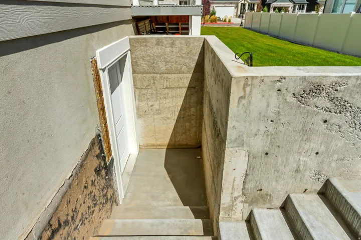 Concrete-walled entryway with a white door, concrete steps, and a grassy perimeter