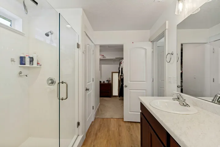 Glass-enclosed shower with chrome fixtures, wood-finish flooring, single vanity with integrated sink, and white paneled doors