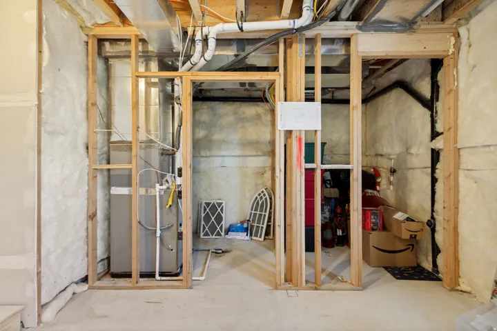 Basement area featuring exposed wood framing, concrete flooring, and an accessible water heater