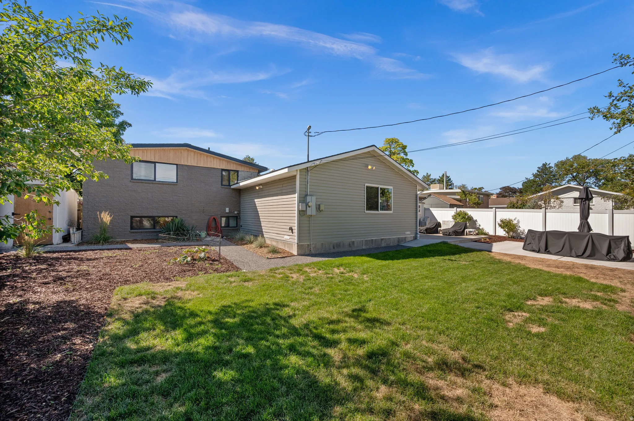 Expansive backyard featuring a manicured lawn, paved patio, gravel pathways, and a white privacy fence