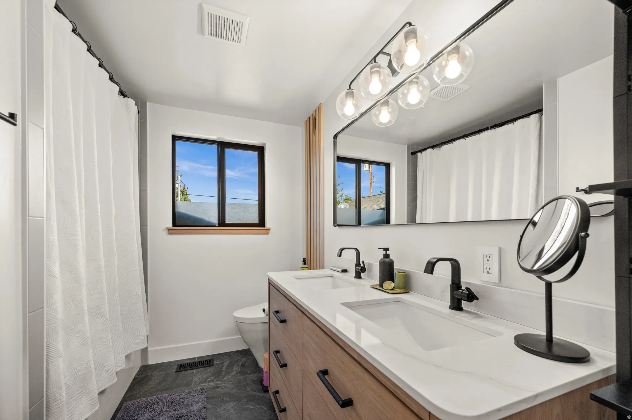 Dual vanity with matte black faucets, wood-finish cabinetry, and white countertops