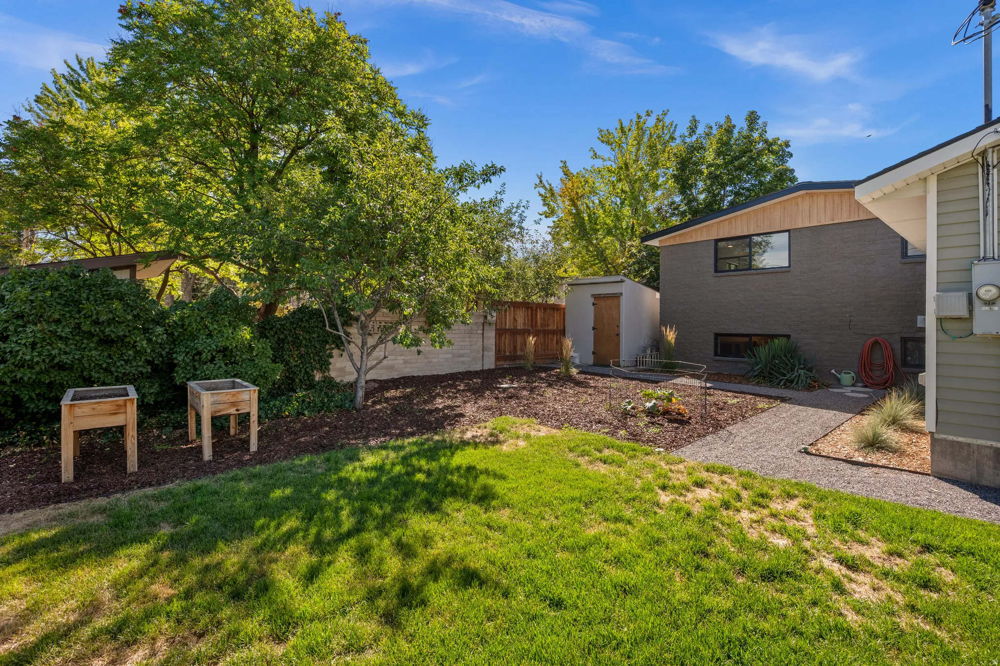 Expansive grassy area with mature trees, gravel pathway, and a detached storage shed