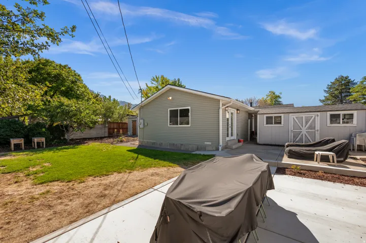 Exterior featuring light green siding, white trim windows, double glass panel doors, a concrete patio, and a separate storage shed