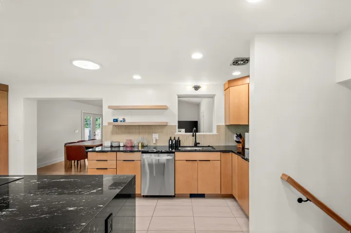 Kitchen featuring light wood cabinetry, black countertops, stainless steel dishwasher, and recessed lighting
