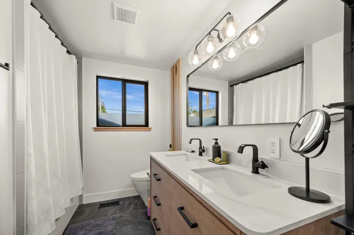 Dual vanity with matte black faucets, wood-finish cabinetry, and white countertops
