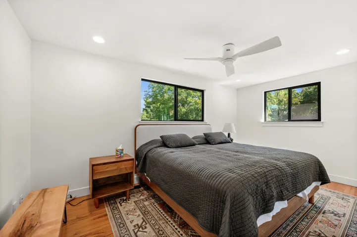 Recessed ceiling lighting, wood-finish flooring, white walls, black-framed windows, and a ceiling fan