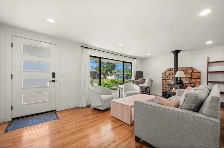 Hardwood flooring throughout, contemporary entry door with frosted glass panels, stone-clad wood-burning stove, large picture windows, and recessed lighting