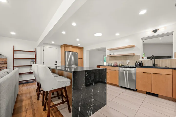 Kitchen featuring a black stone island, stainless steel appliances, light wood-finish cabinetry, and recessed lighting