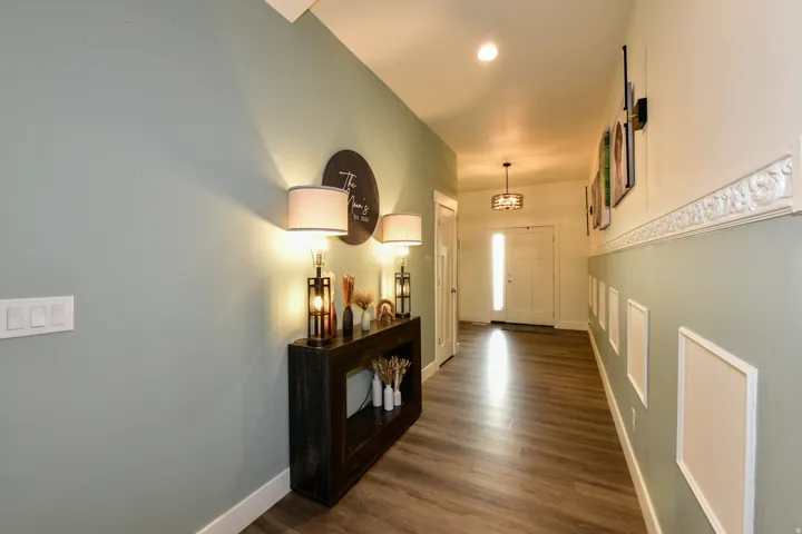 Wood-finish flooring throughout, light green and white painted walls, decorative wall molding, recessed ceiling lighting, and a chandelier-style ceiling fixture