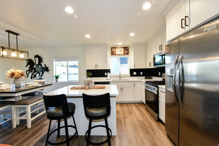 Kitchen featuring white cabinetry, a center island with countertop seating, stainless steel appliances, wood-finish flooring, and a dining area with a linear chandelier