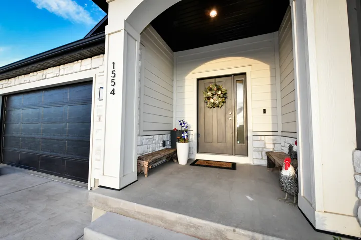 Covered front porch with concrete flooring and exterior lighting, featuring a dark-paneled entry door with a sidelight