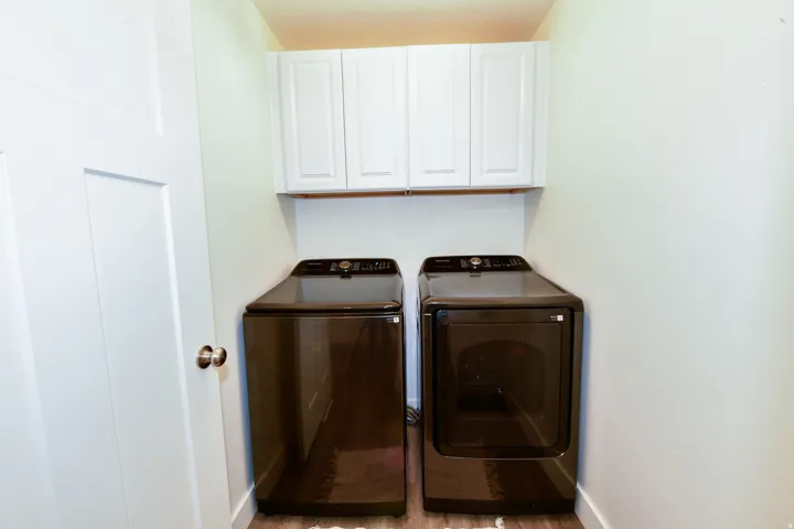 White shaker-style cabinetry with a wood-finish shelf, above a dark-finish washer and dryer set, all set on wood-finish flooring