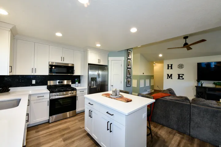 Well-appointed kitchen featuring white cabinetry, stainless steel appliances, a black tile backsplash, wood-finish flooring, and a center island with a white countertop
