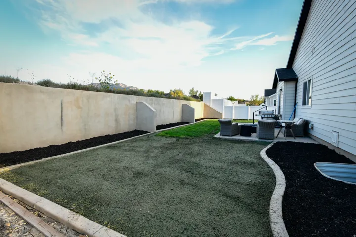 Expansive backyard featuring a concrete patio, retaining wall, and manicured lawn