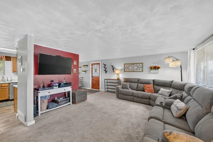 Carpeted living area with light gray walls, a red accent wall, and a wood-finish entry door with frosted glass panels
