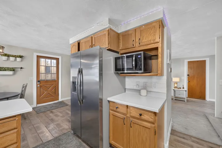 Kitchen featuring wood-finish flooring, oak cabinetry, stainless steel refrigerator, and white countertops with a subway tile backsplash