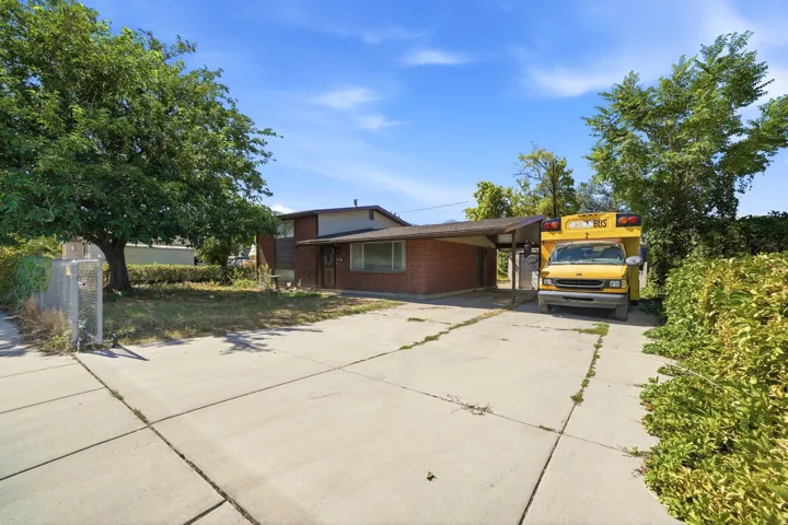 Red brick exterior, covered carport, concrete driveway, mature trees, and established landscaping