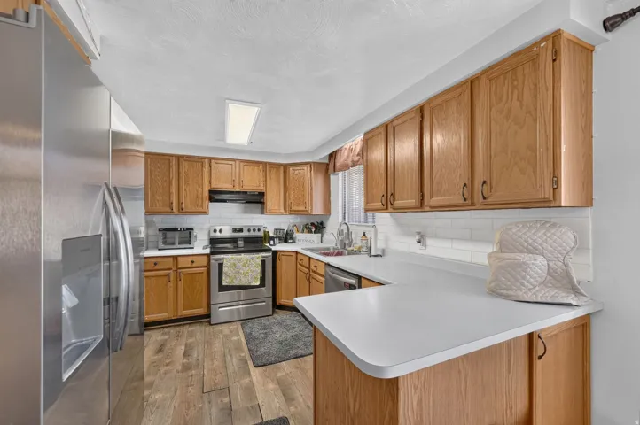 Kitchen featuring light wood cabinetry, white countertops, stainless steel appliances, and a white subway tile backsplash